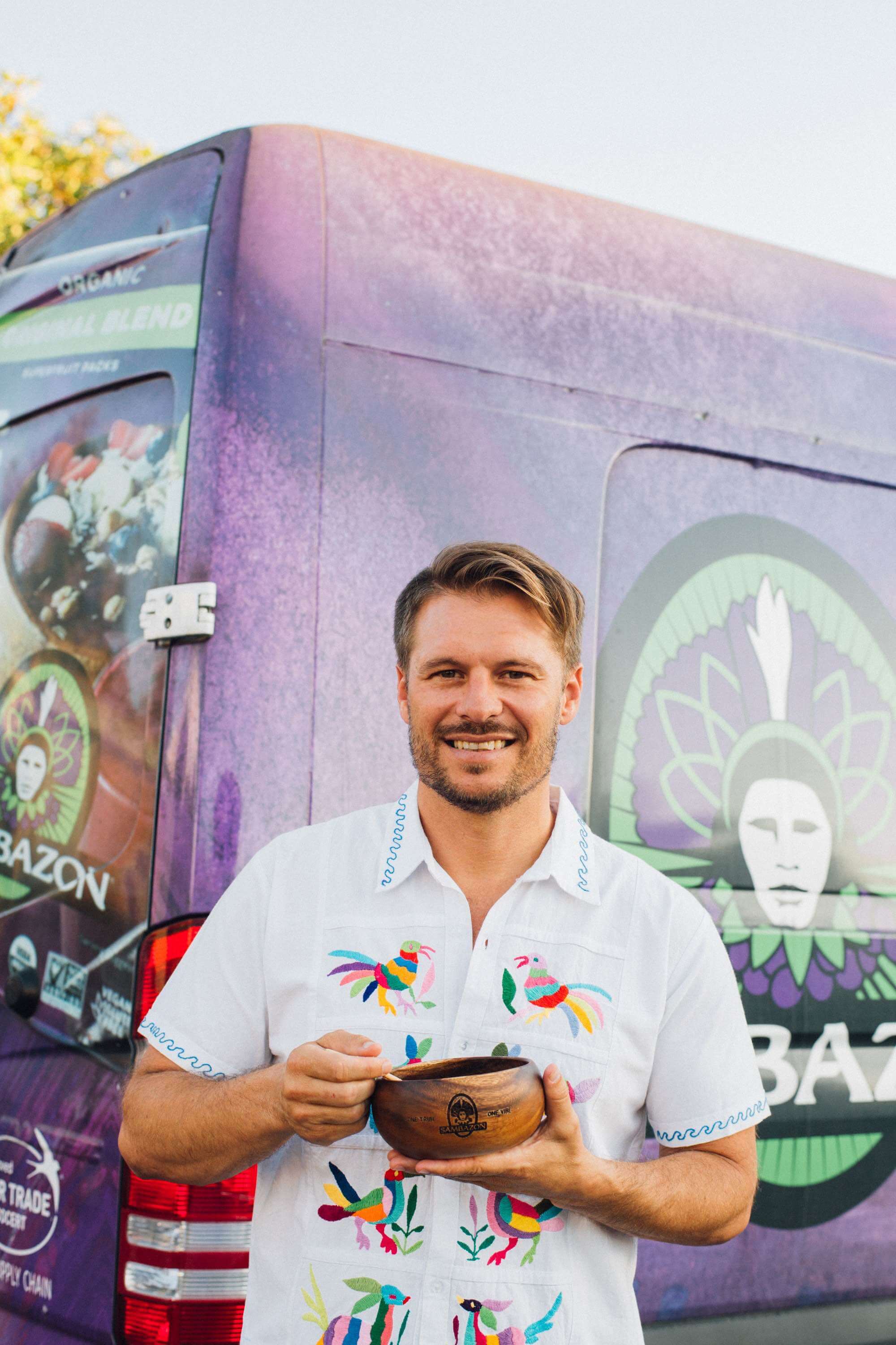 Ryan Black holding an açaí bowl in front of a purple SAMBAZON vehicle