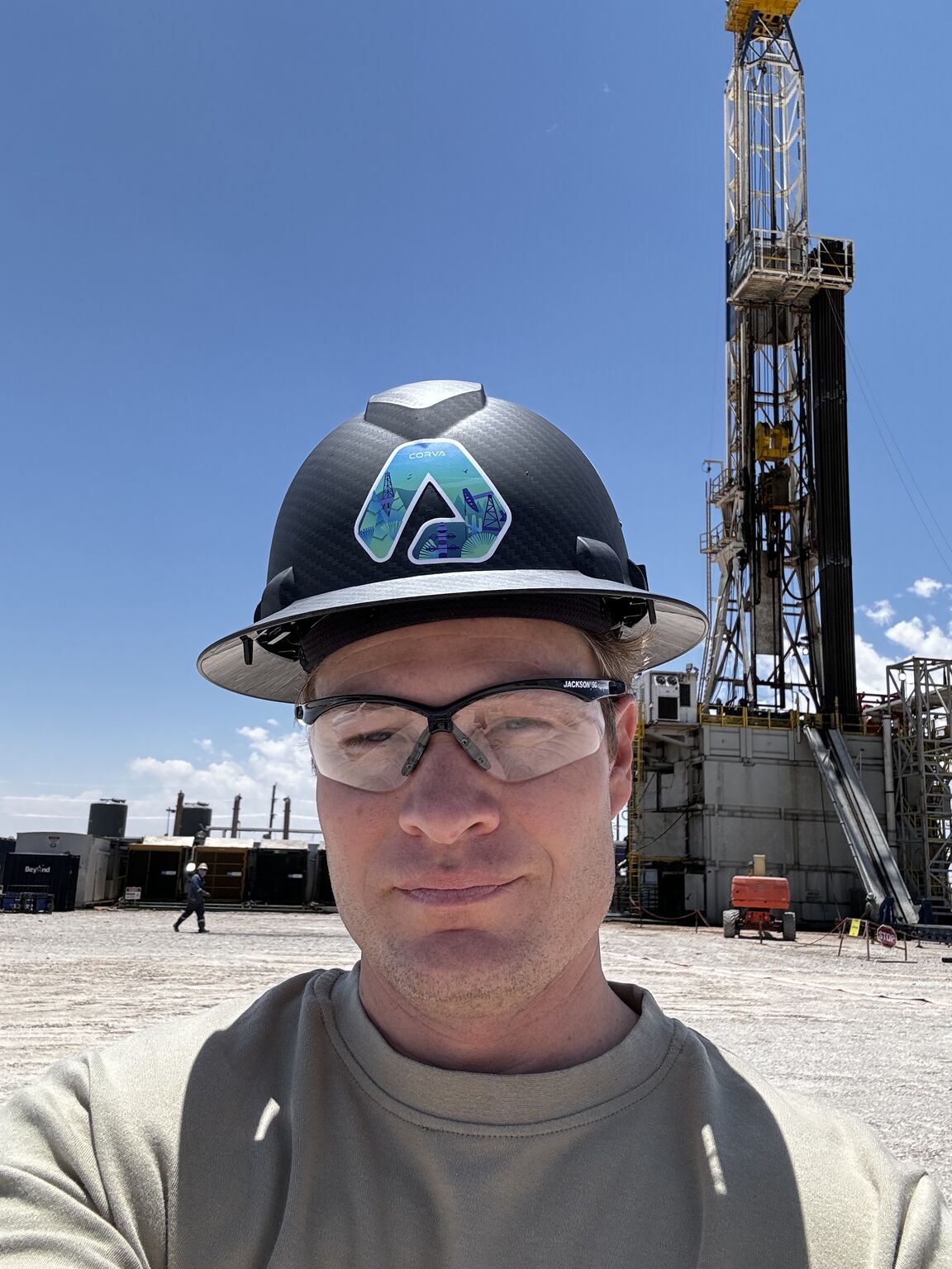 Ryan Dawson wearing a Corva hard hat and protective glasses with a drilling rig behind him