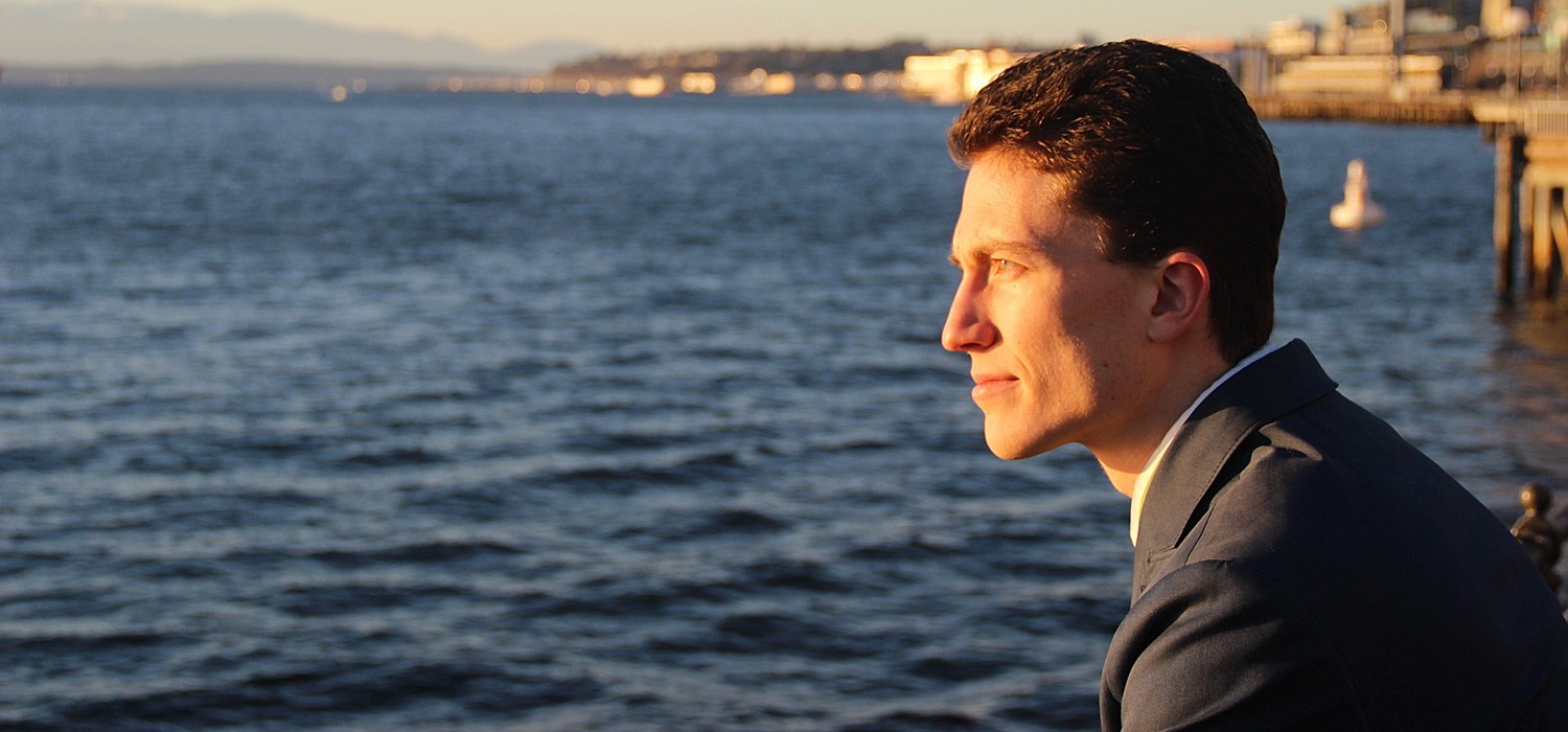 Ryan Vogel seated beside a large body of water at sunset