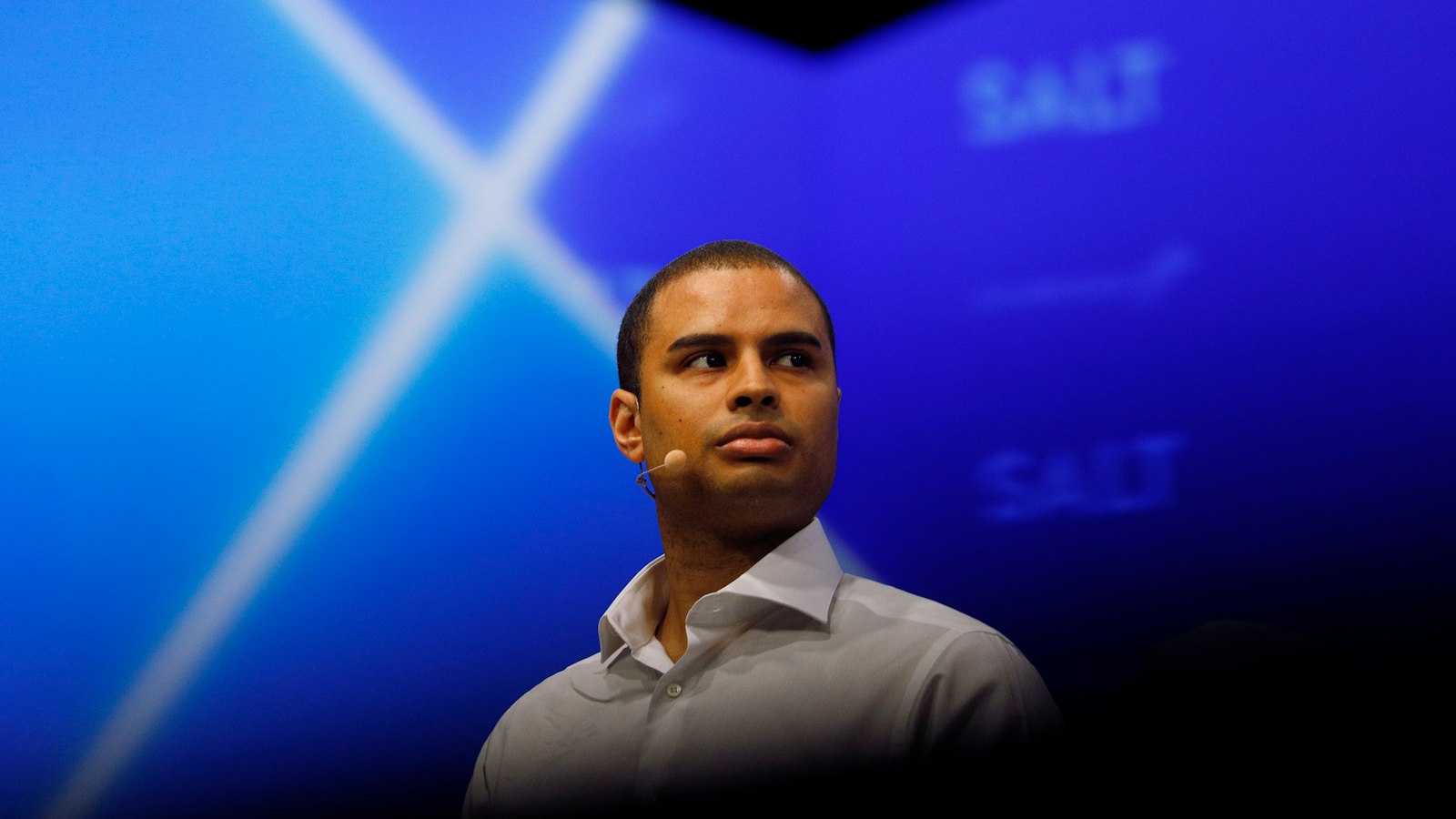 Ryan Williams wearing a headset microphone on a blue-lit conference stage