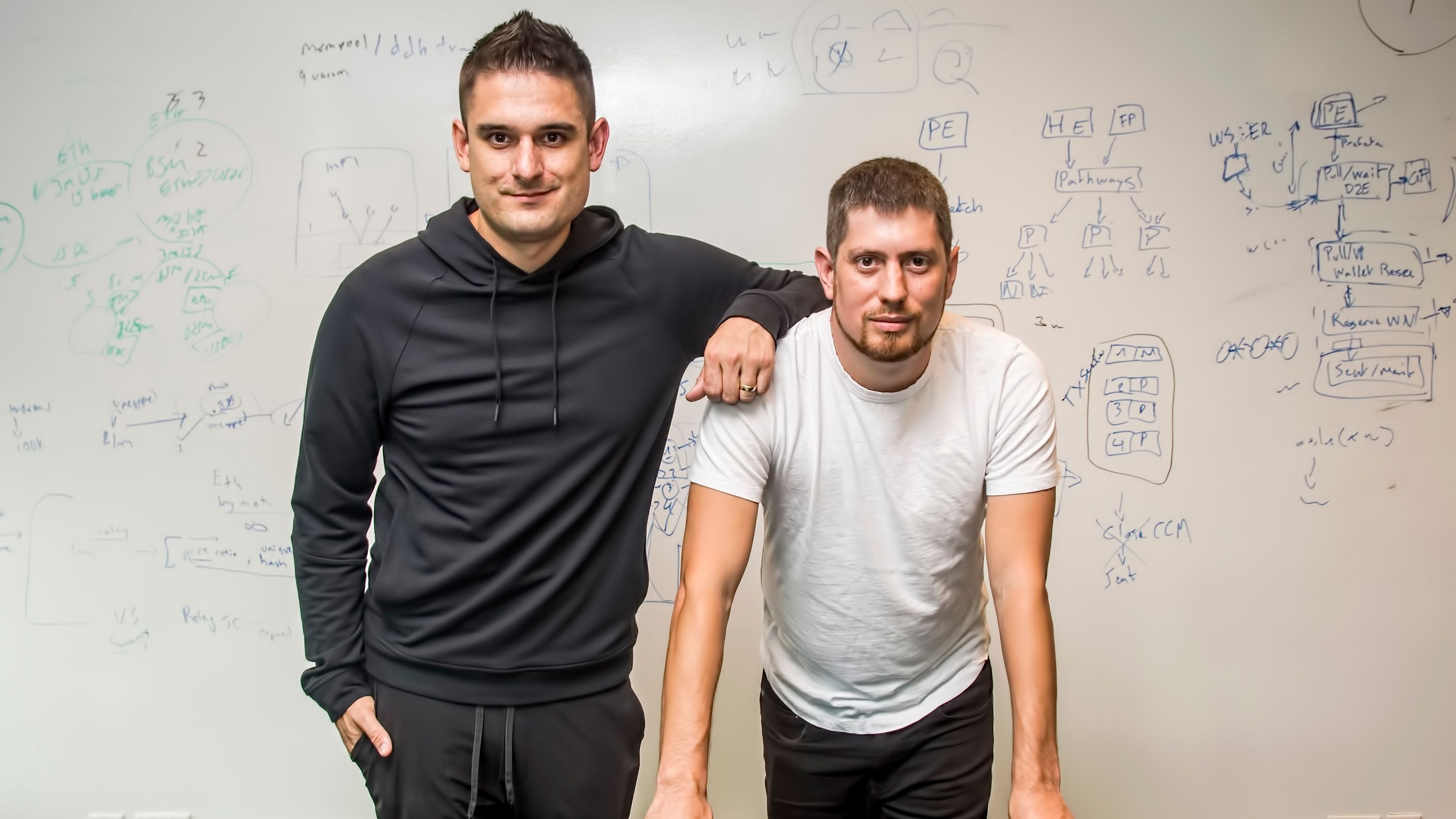Ryan Zarick and Bryan Pellegrino in front of a whiteboard covered with technical sketches