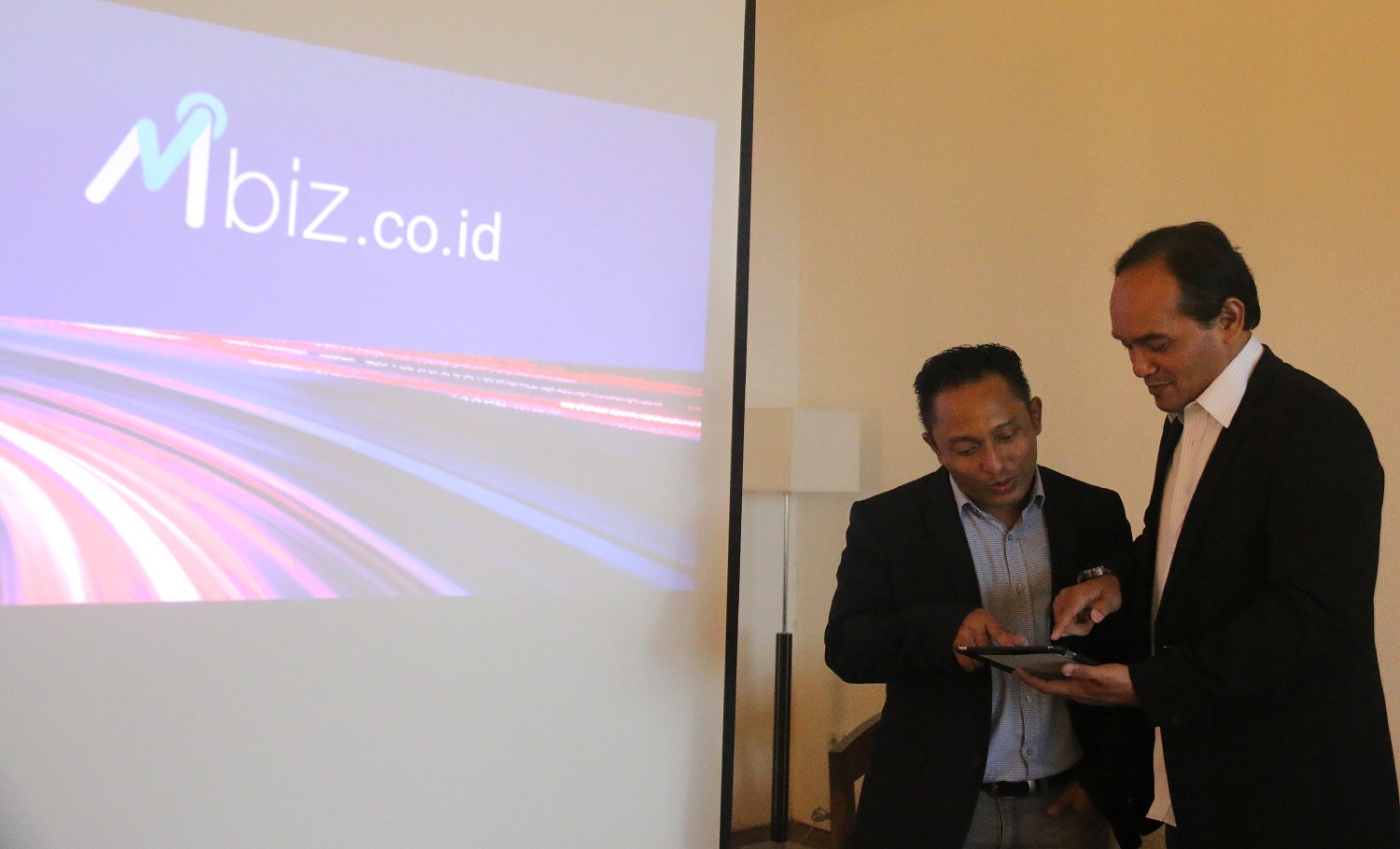 Ryn Hermawan, left, and Andik Duana Putra looking at a tablet beside an Mbiz projection