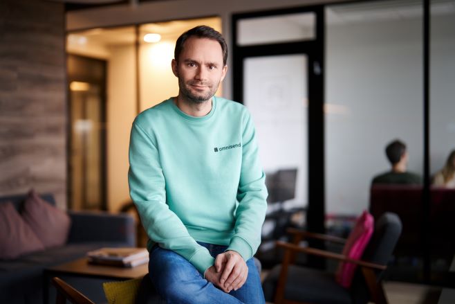 Rytis Lauris seated in an Omnisend office, wearing a mint-green sweatshirt