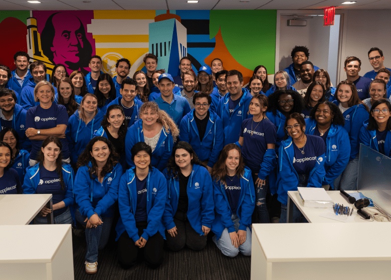 Applecart colleagues gathered in blue company clothing in front of a colorful office mural