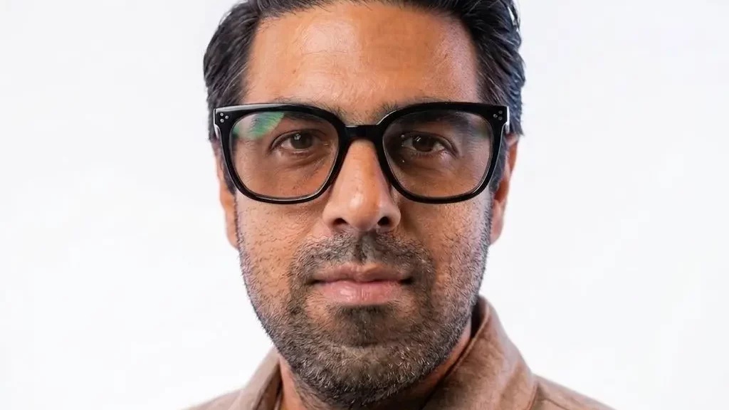 Sachin Dev Duggal wearing dark-framed glasses in a press photograph
