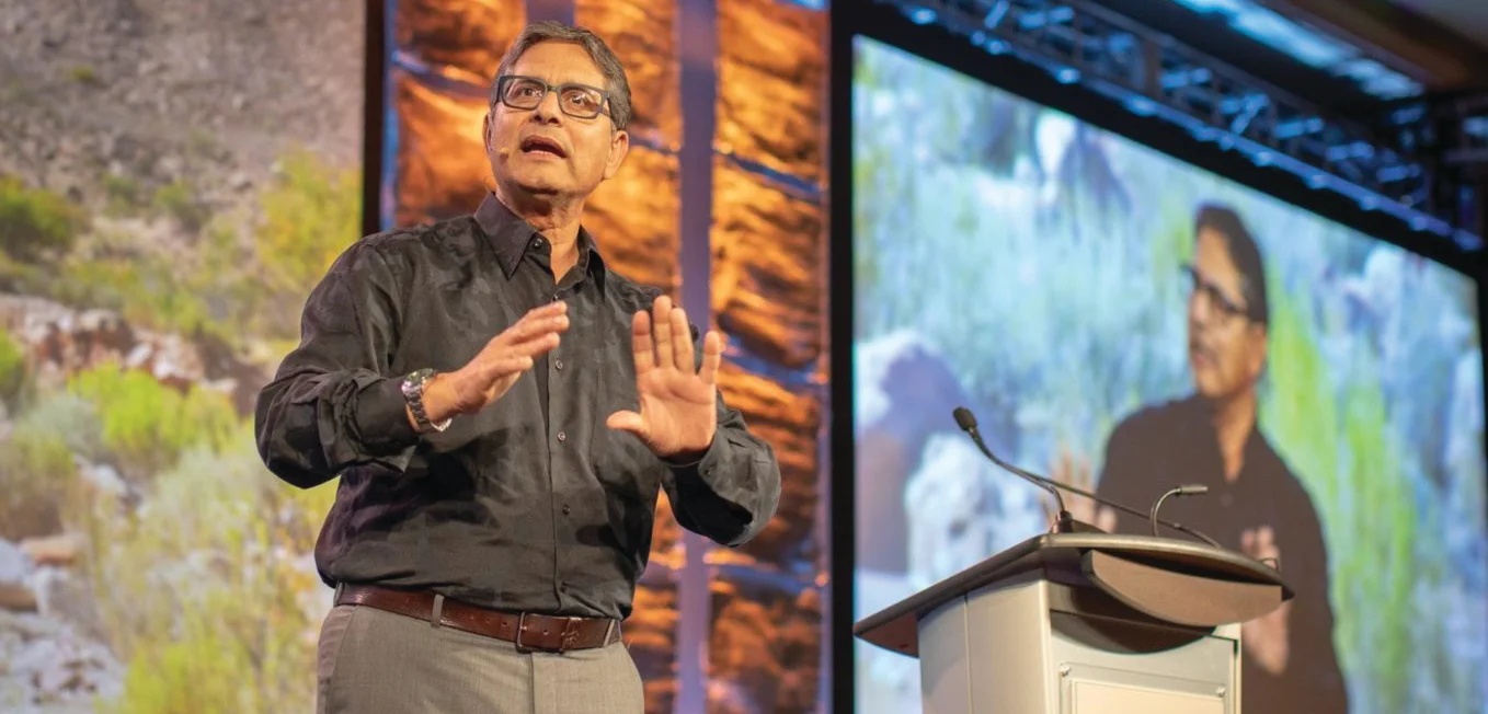 Safwan Shah speaking onstage beside a lectern, with his image projected behind him