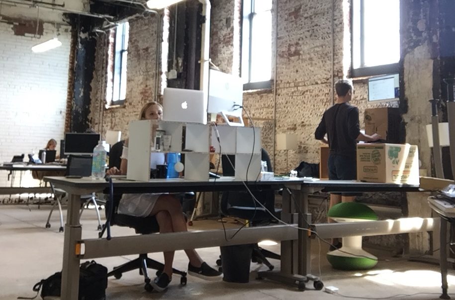The Compass office in 2017, with tall windows, exposed brick, desks and computer monitors.