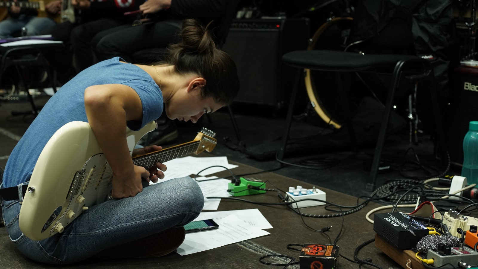 A GSUBI guitarist adjusting her instrument among scores, cables and effects pedals in 2020