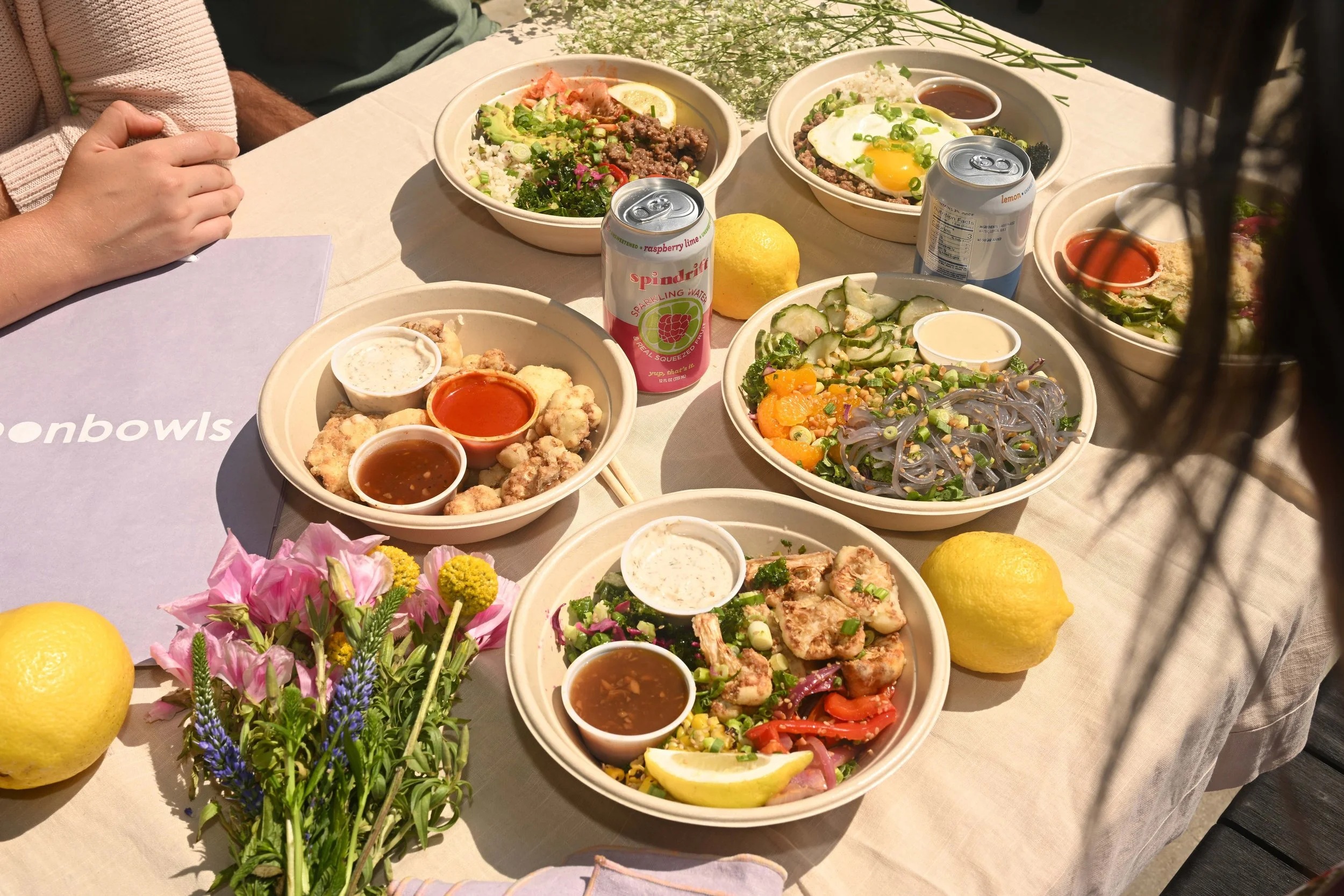 moonbowls bowls, cauliflower sides, sauces, and drinks spread across a sunny outdoor table