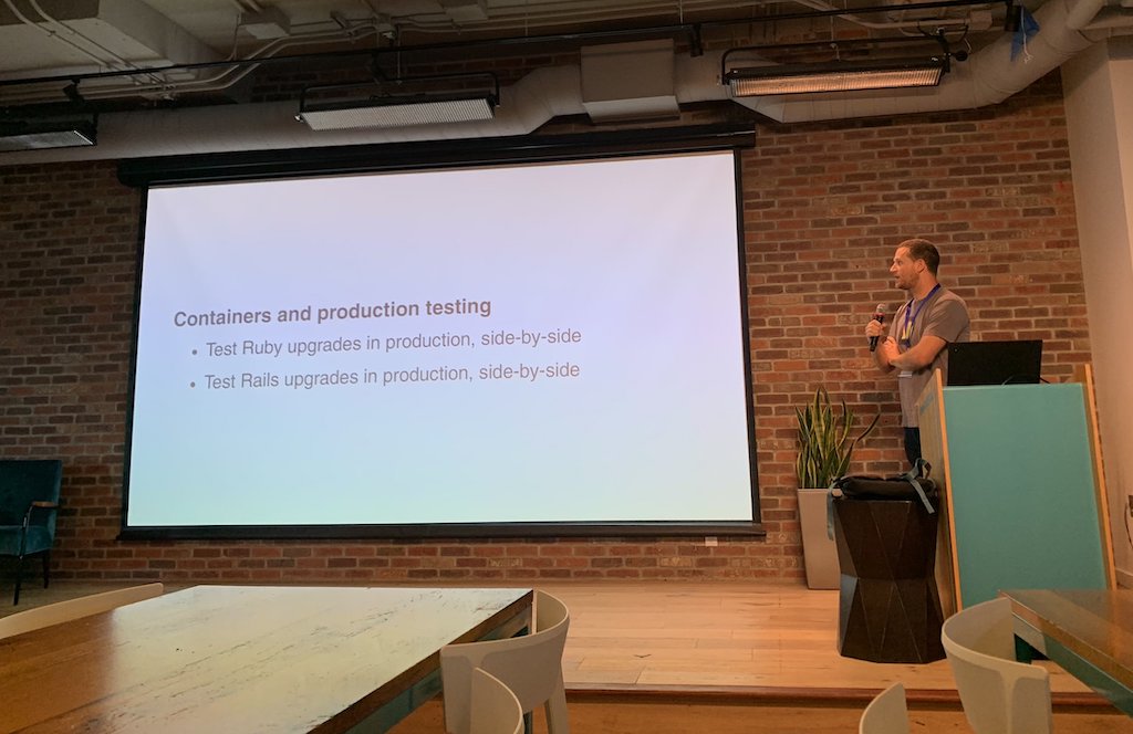 Sam Saffron holding a microphone beside a presentation on containers and production testing at Shopify in Ottawa