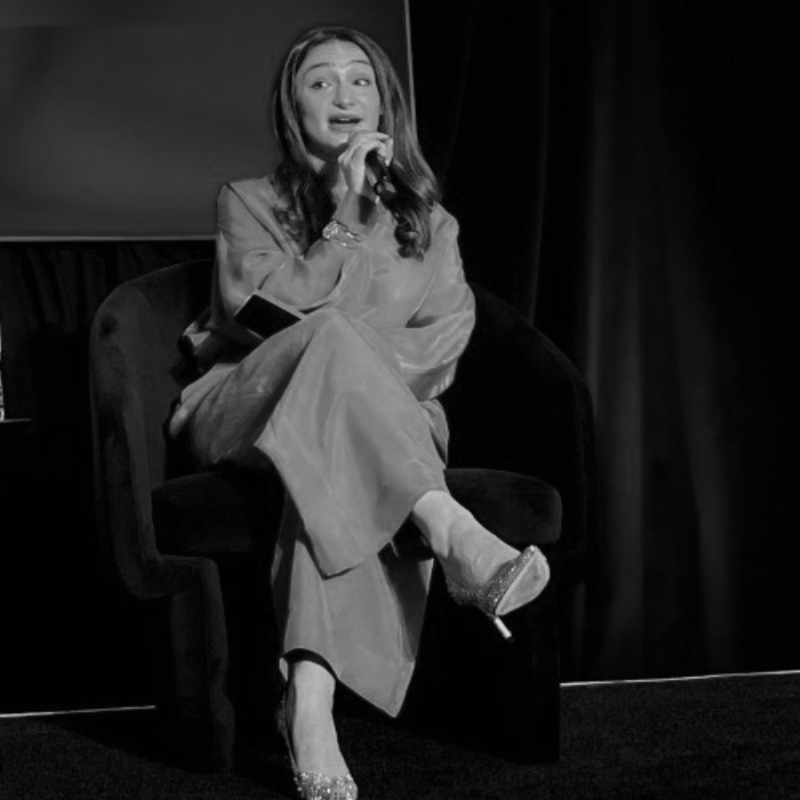 Samantha Citro Alexander seated onstage, speaking into a handheld microphone