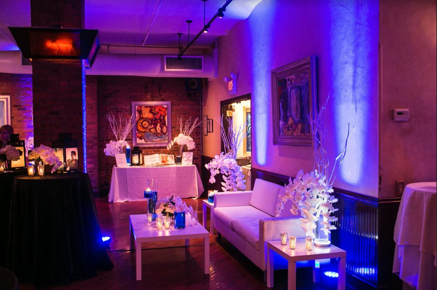 An event lounge with white seating, floral arrangements, framed art, and purple lighting