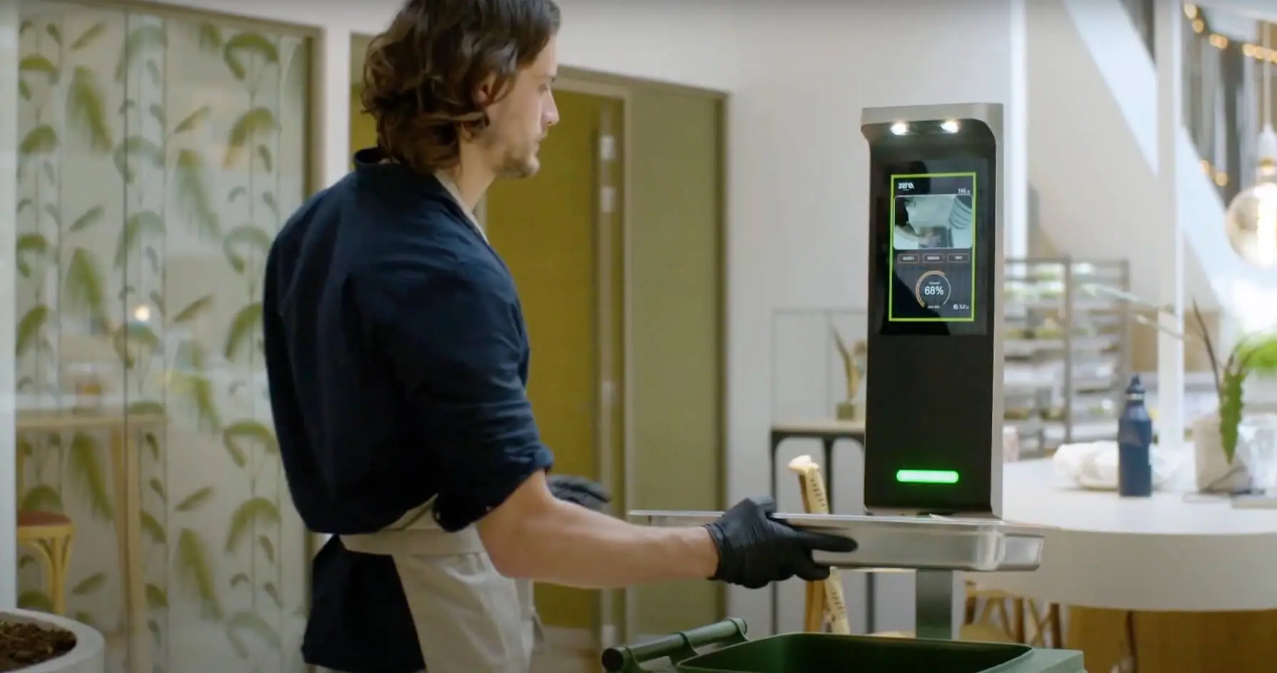A restaurant worker using an Orbisk food-waste monitor above a collection bin