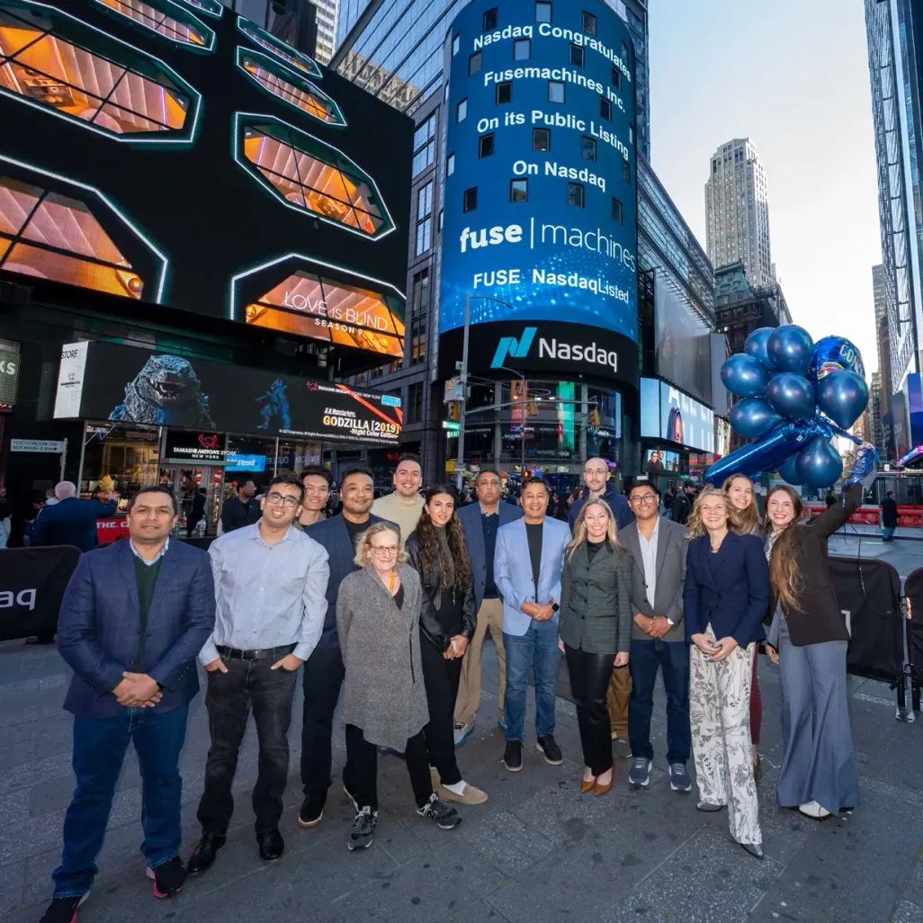 Sameer Maskey, wearing a pale blue blazer near the center, with the Fusemachines team beneath a Nasdaq congratulations display in Times Square