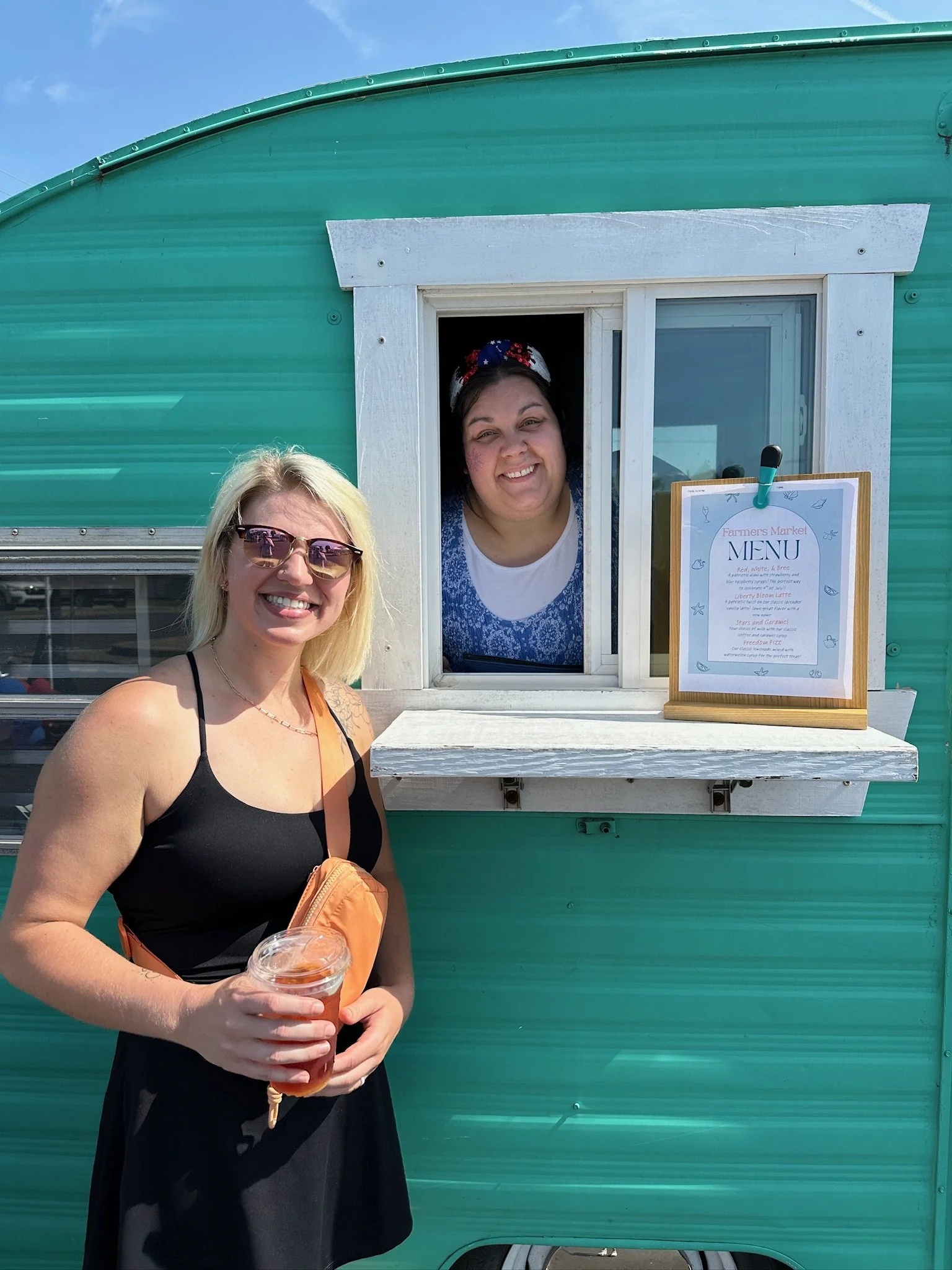 Sami Brown holding a drink beside a turquoise food-trailer serving window, with another person smiling inside.