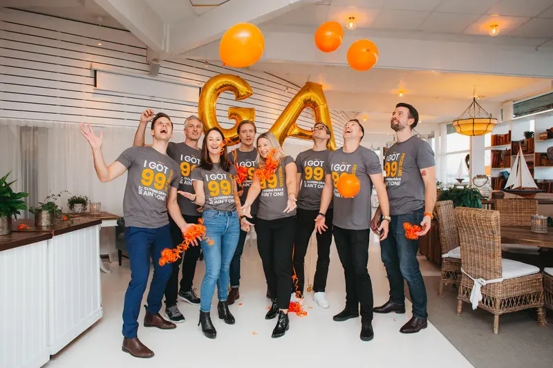 GetAccept colleagues under orange balloons, wearing matching shirts and celebrating together in an office