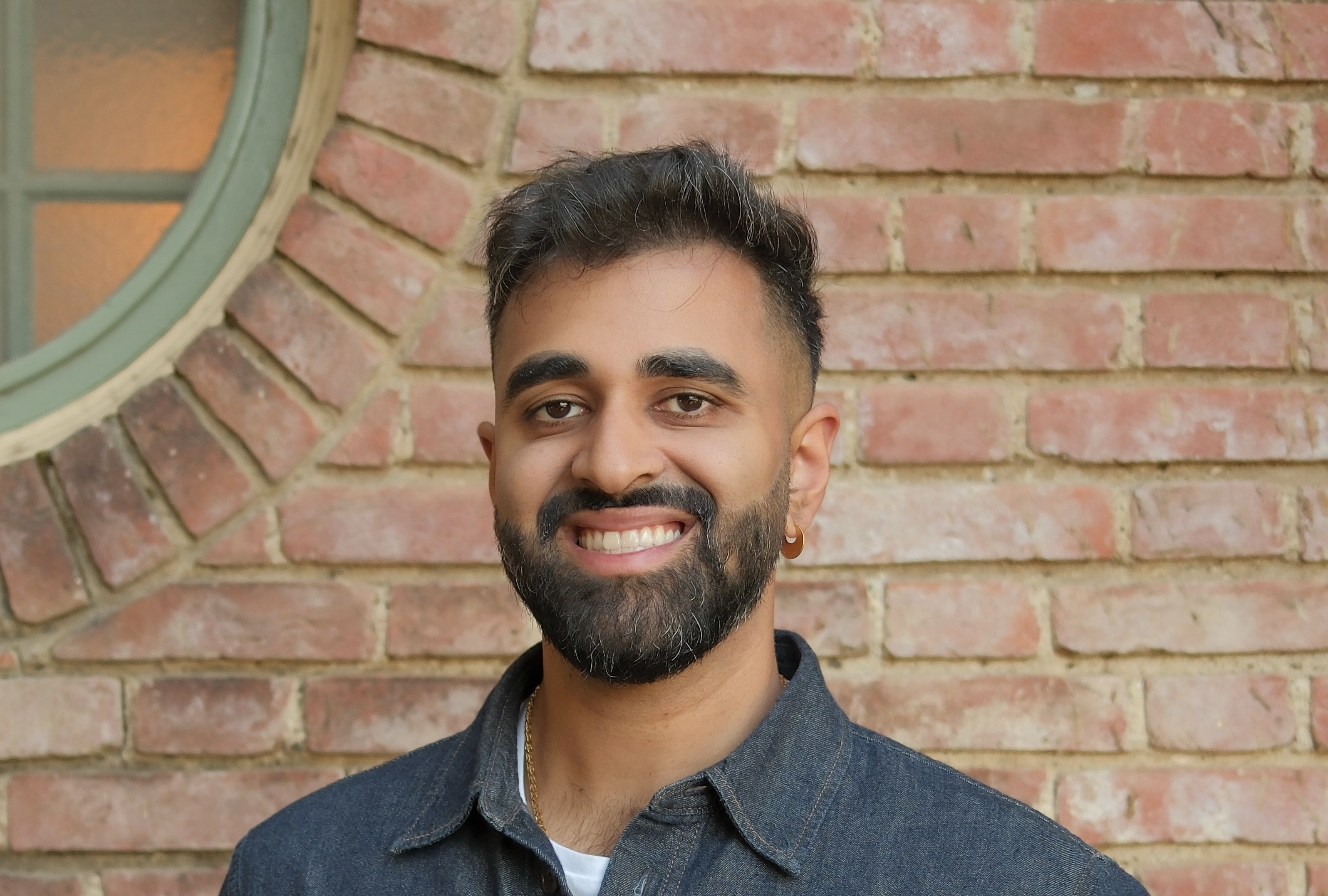 Samraaj Bath smiling in front of a brick wall