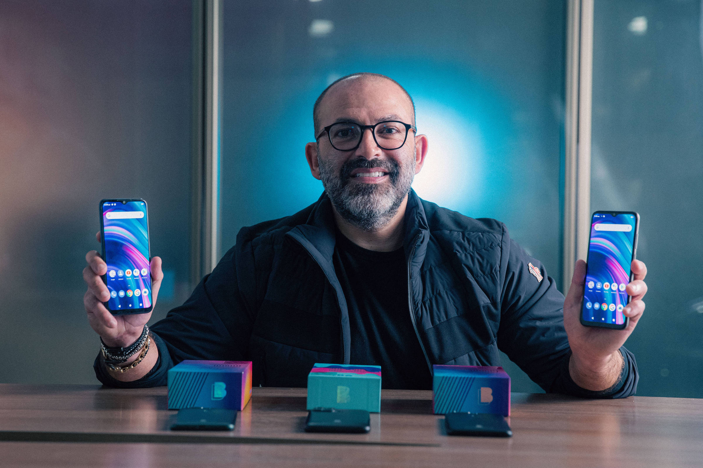 Samuel Ohev-Zion holding two BLU smartphones behind three phone boxes in 2022