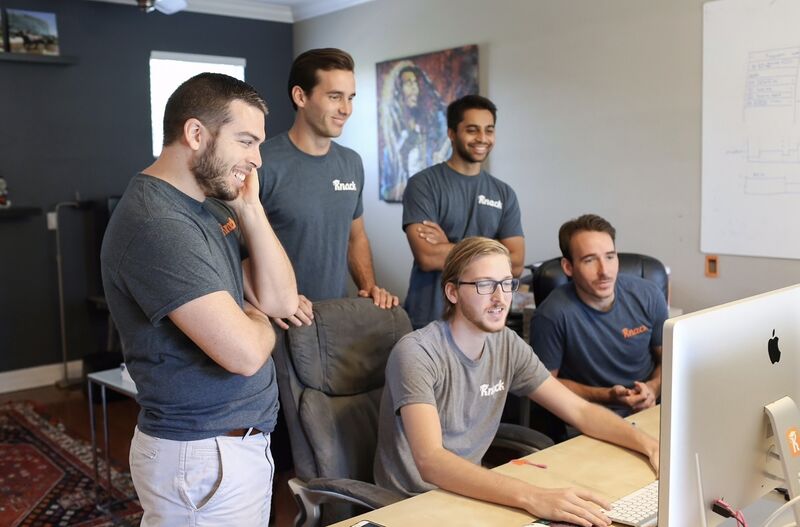 Early Knack team gathered around a desktop computer; Samyr Qureshi stands at the back with his arms folded