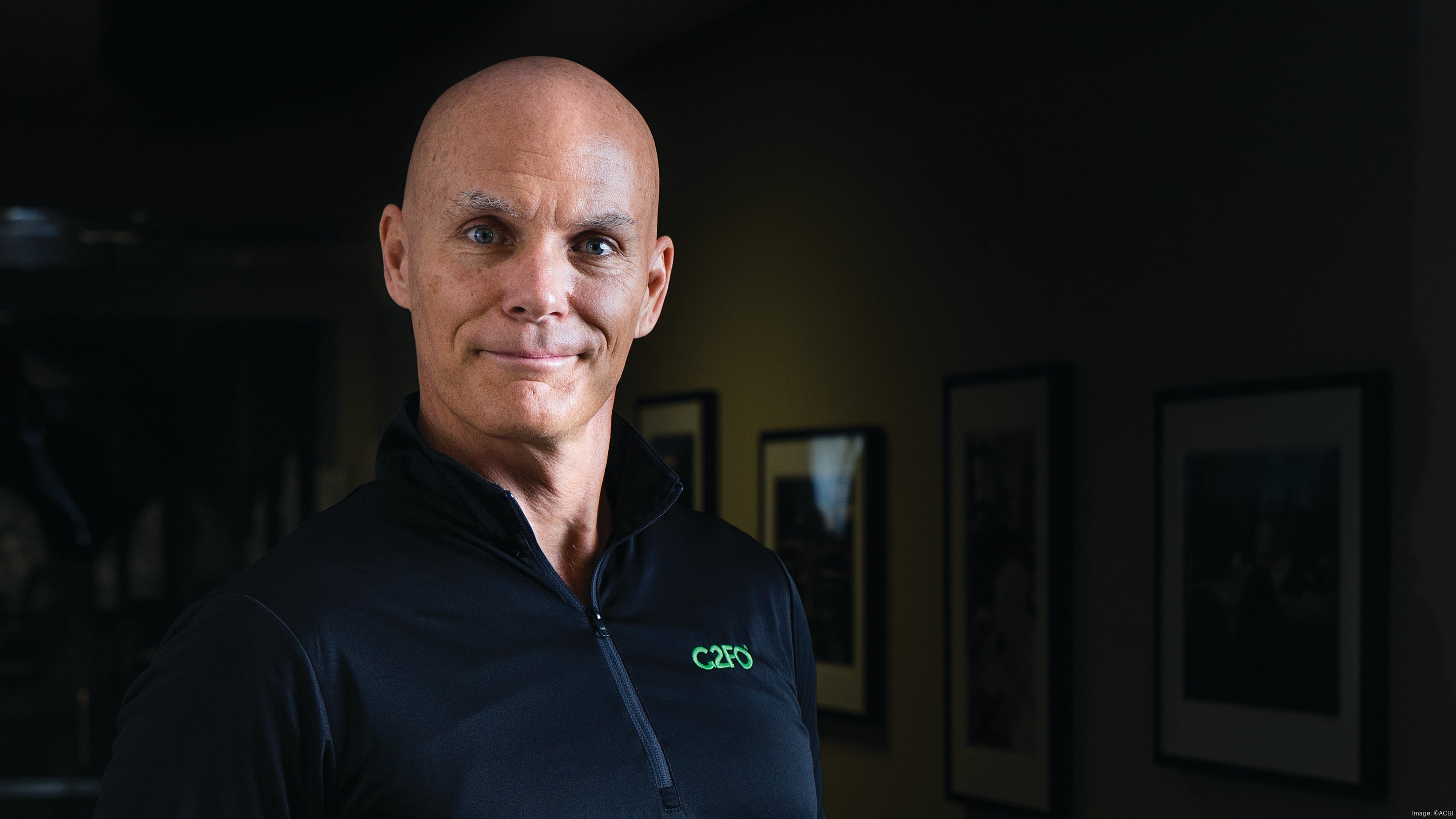 Sandy Kemper wearing a C2FO jacket, with framed artwork behind him