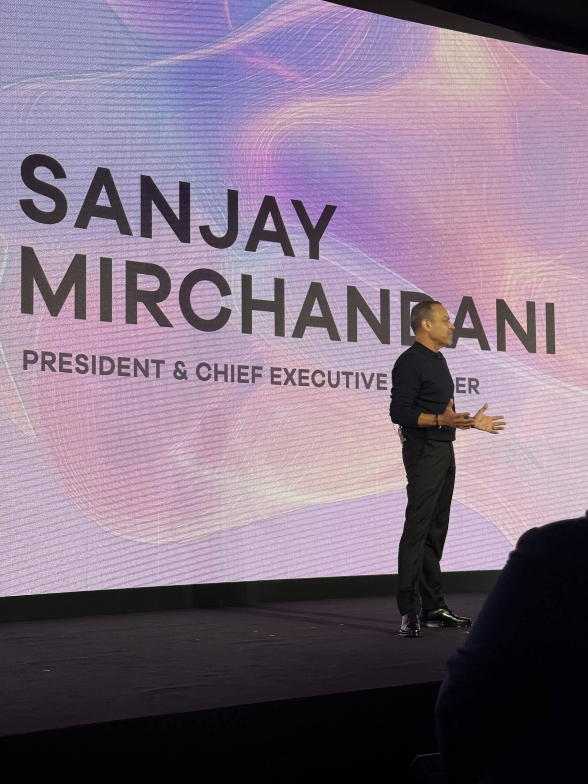 Sanjay Mirchandani speaking onstage at Commvault SHIFT in London, with his name projected behind him