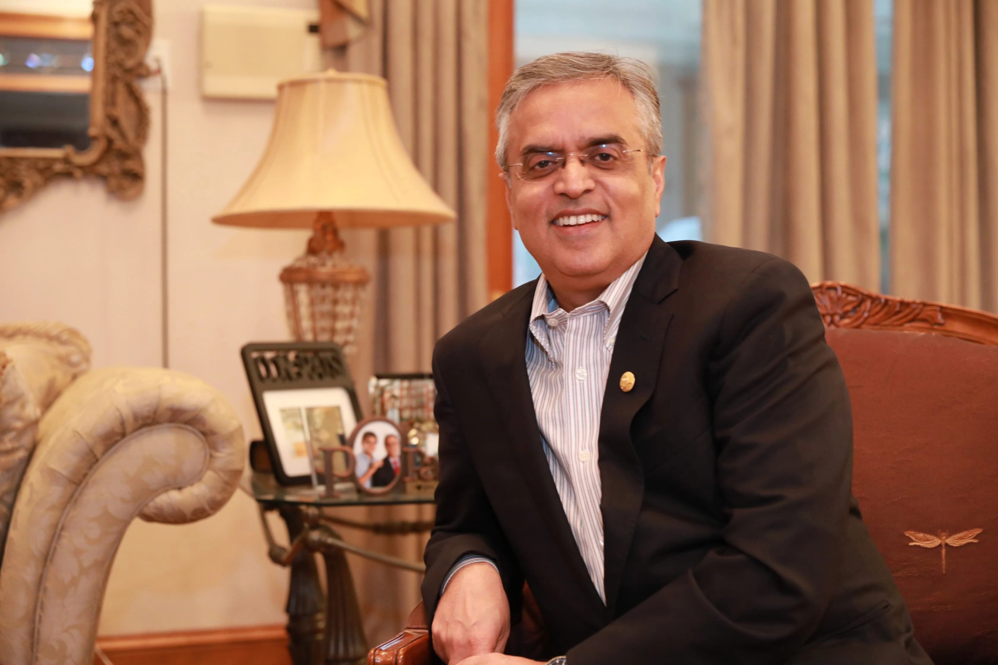 Sanjay Sehgal seated indoors, smiling in a dark jacket