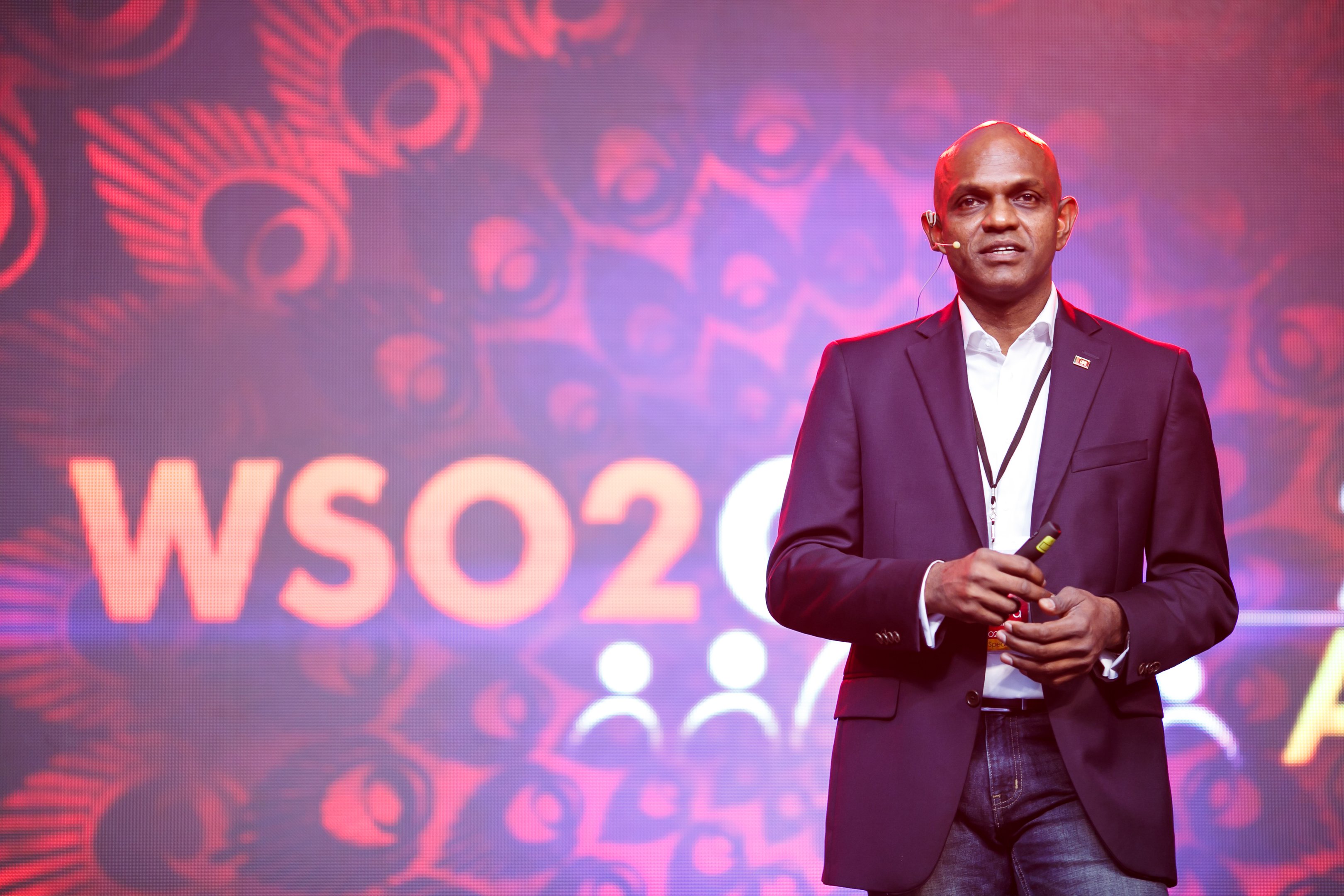Sanjiva Weerawarana speaking on a WSO2 stage, holding a presentation remote
