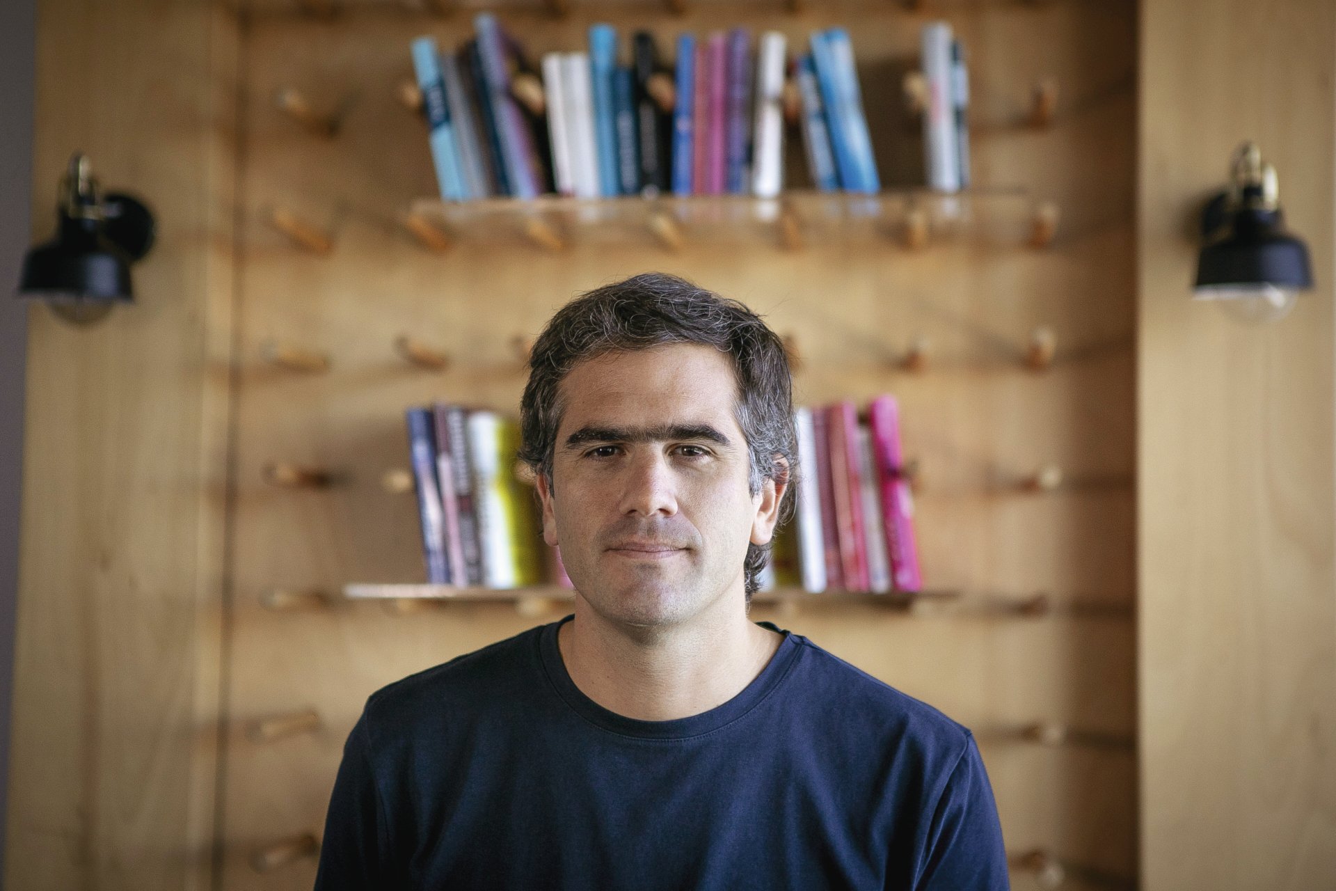 Santiago Zabala in a navy shirt, photographed in front of wooden bookshelves