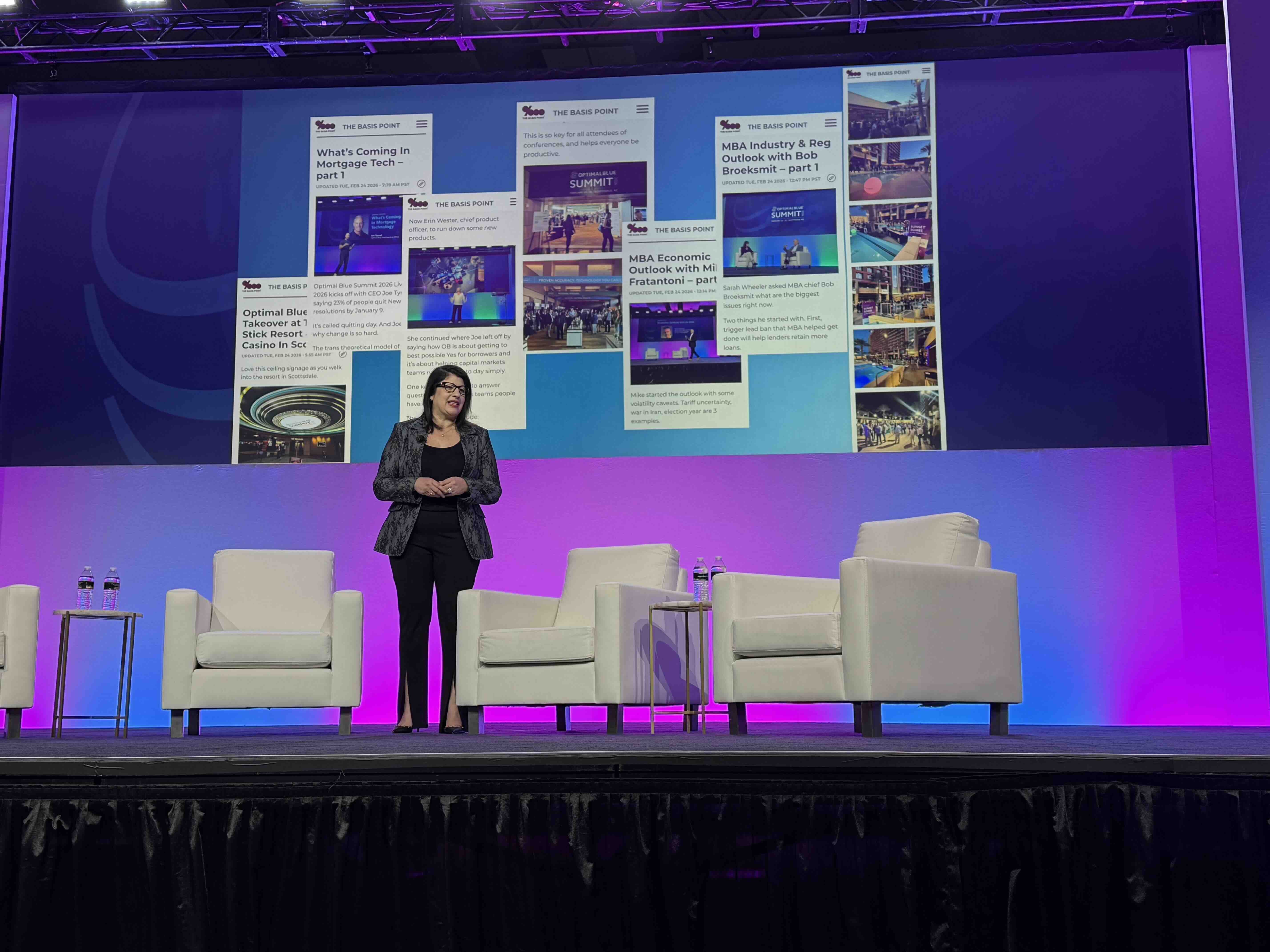 Sara Holtz standing onstage at Optimal Blue Summit 2026 with a live-blog display behind her