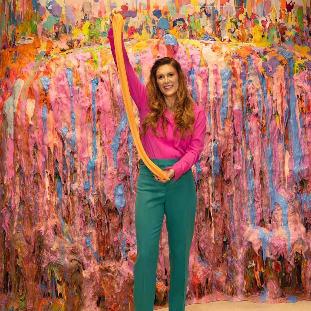 Sara Schiller stretches orange slime against a wall layered with colorful slime