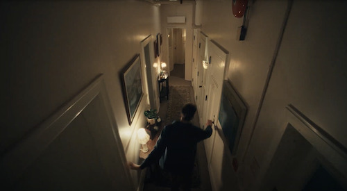 A cinematic overhead frame from The Maze campaign showing a person moving through a dim interior corridor
