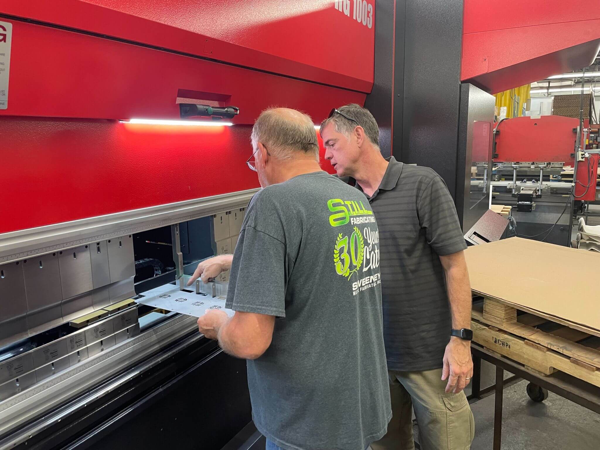 Two manufacturing professionals inspect a large red sheet-metal press at Sweeney Metal Fabricators