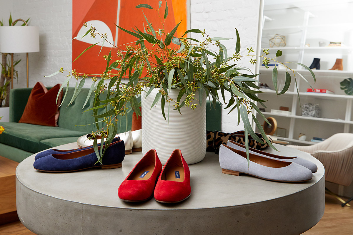 Red, blue, and pale gray ballet flats arranged around flowers on a circular table in the Margaux office