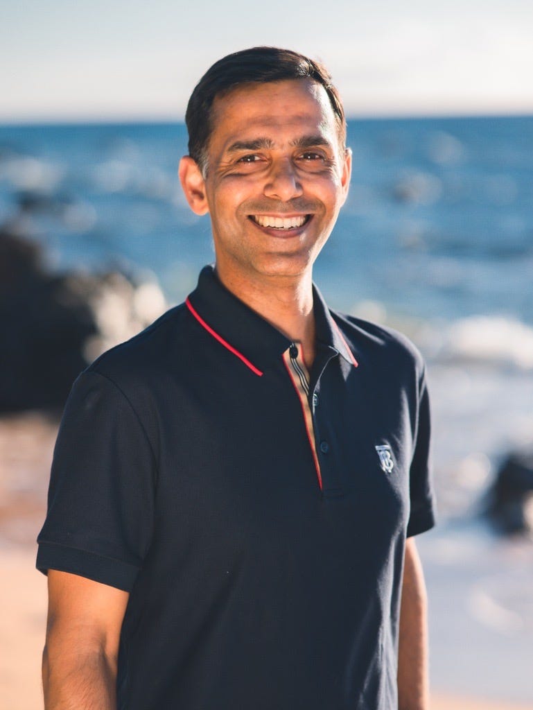 Satish Kumar smiling in a dark polo shirt near the coast