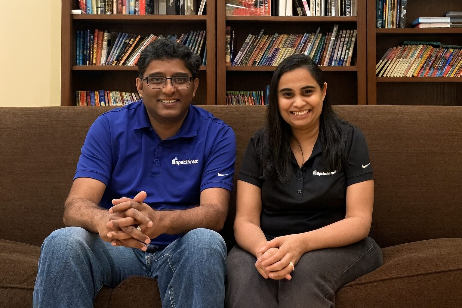 Satish Natarajan, left, and Shailu Satish sitting together on a couch in front of bookshelves
