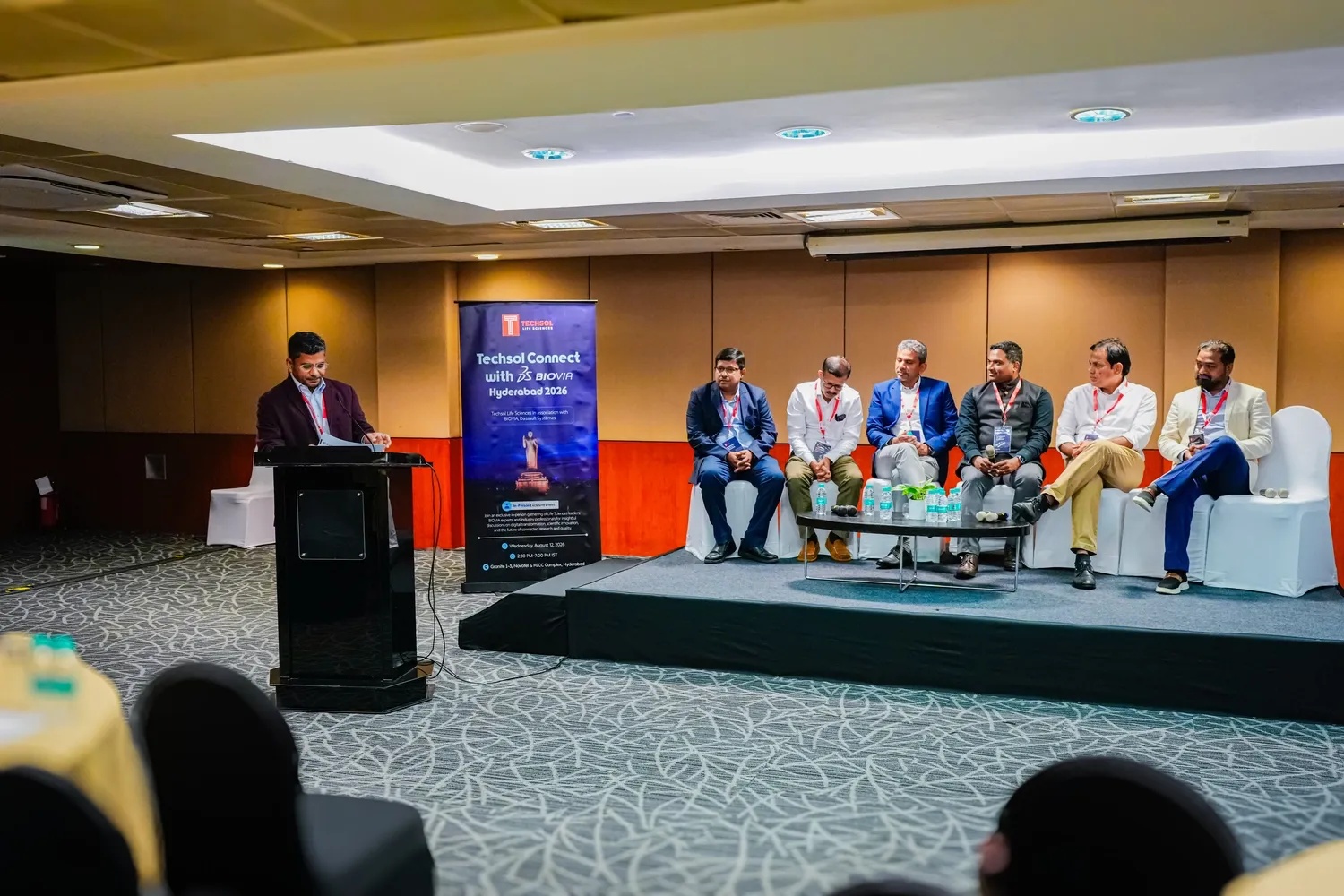 Satya Sagi at a lectern beside a seated panel at Techsol Connect with BIOVIA in Hyderabad