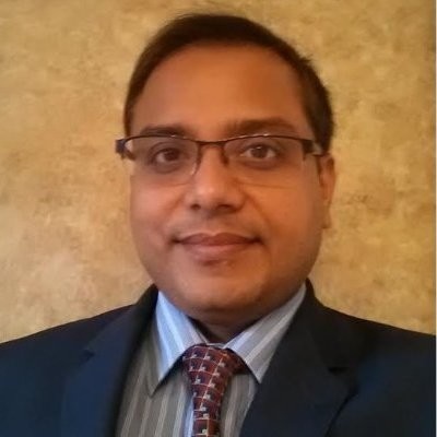 An earlier professional photograph of Saurav Basu wearing glasses, a suit and tie