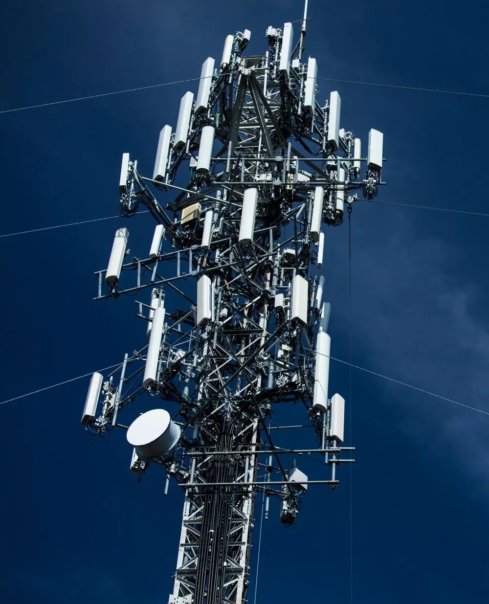 A steel communications tower carrying multiple antenna arrays against a deep blue sky
