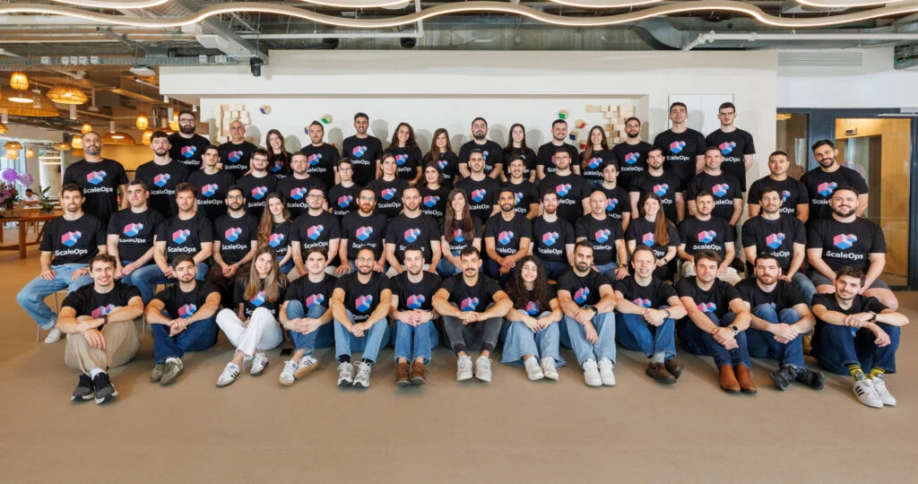 ScaleOps team gathered in an office wearing company shirts