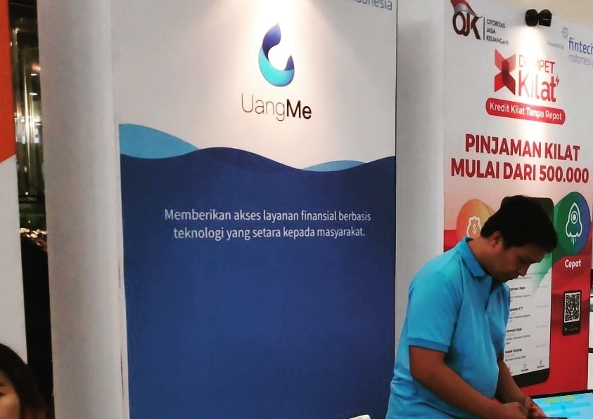 A UangMe exhibition stand at Fintech Days 2018, with a staff member at the counter