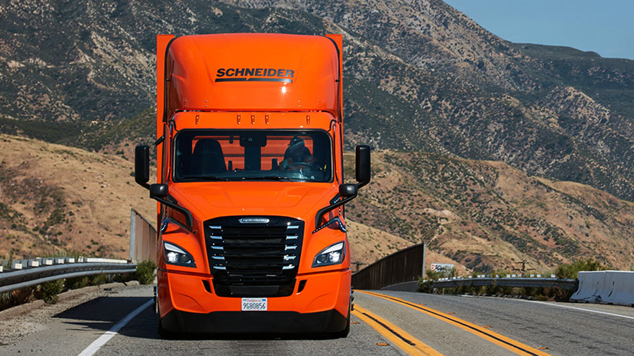 An orange Schneider Freightliner eCascadia electric truck on a California highway