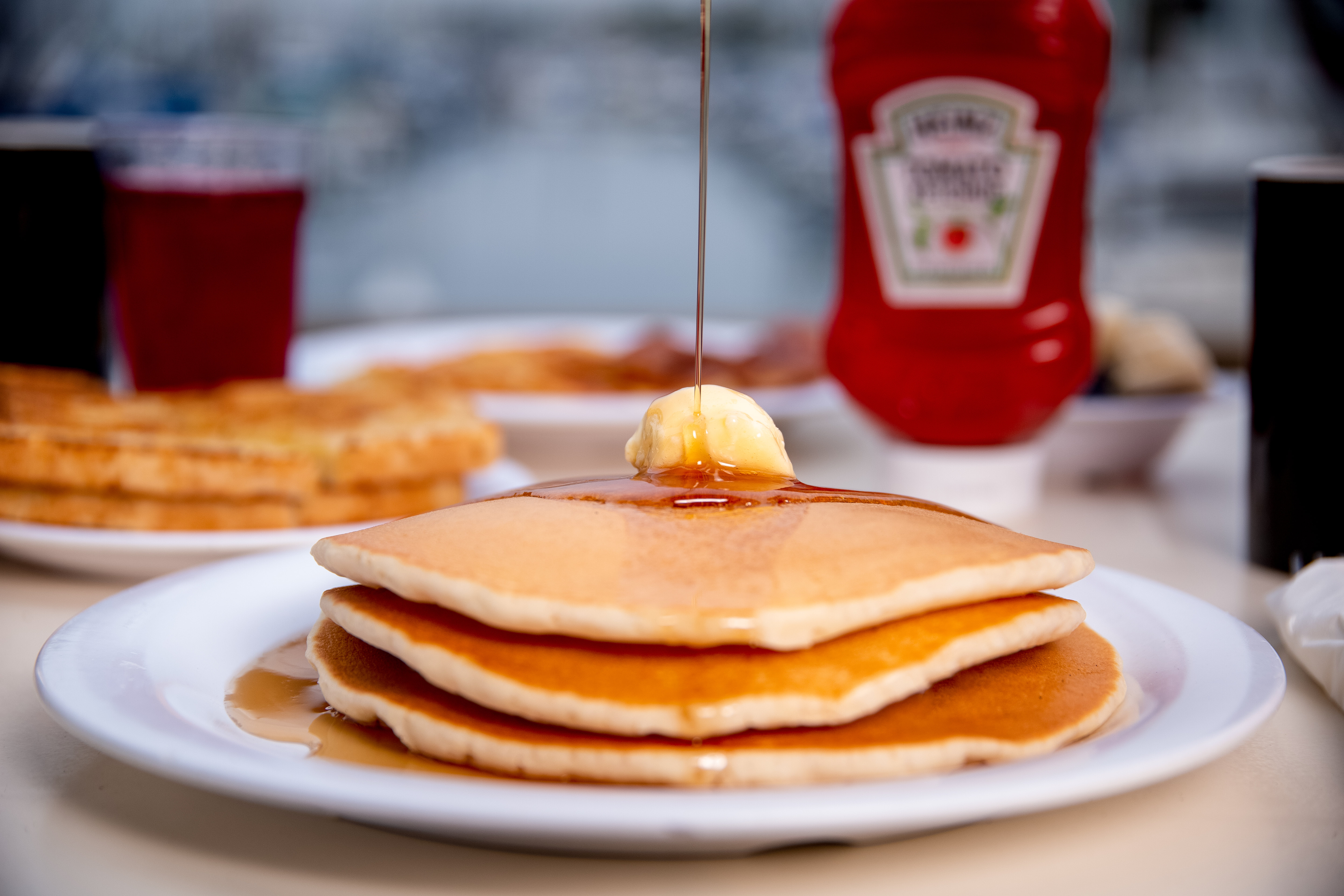A stack of pancakes at Schooner or Later as syrup falls onto butter