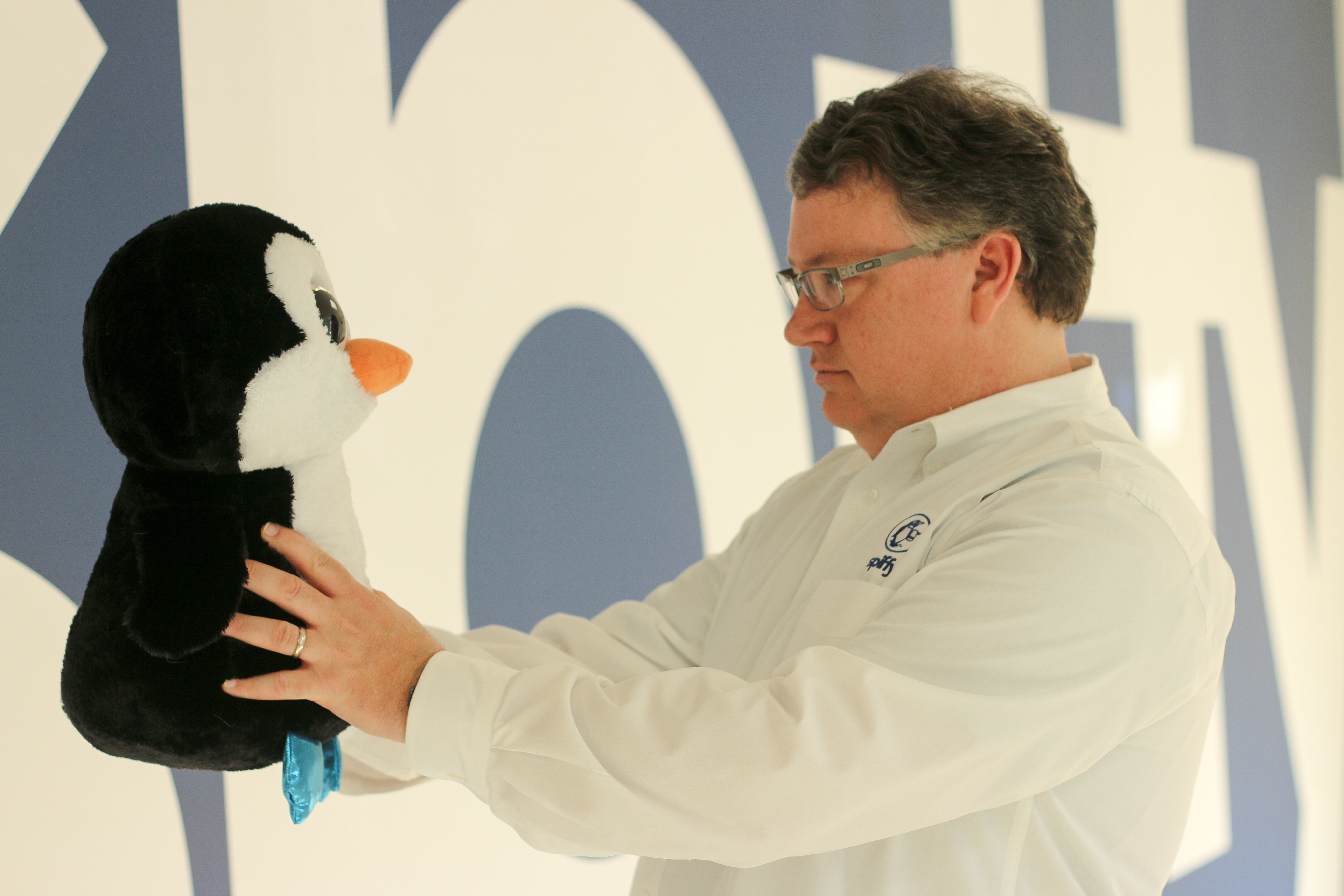 Scot Wingo holding Spiffy’s penguin mascot in front of a branded backdrop