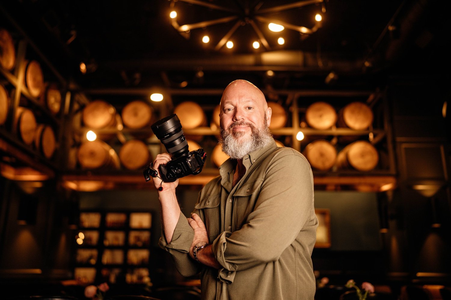 Scott Greenwell holding a camera in a warmly lit room with barrels