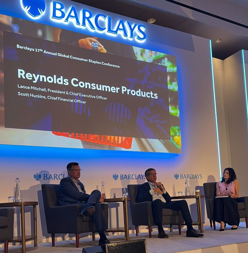 Reynolds executives onstage at the Barclays consumer conference in Boston, with a screen naming Lance Mitchell as CEO and Scott Huckins as CFO