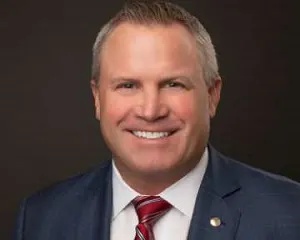 Scott McPherson in an archival PFG press photograph, wearing a suit and red striped tie