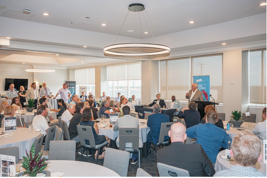Scott Riley holding a microphone while speaking to entrepreneurs seated at round tables at Tampa’s Centre Club