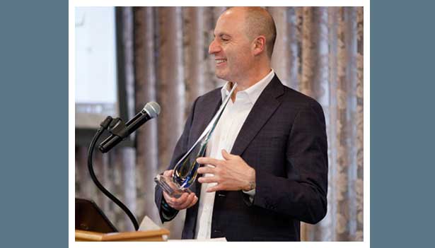 Scott Salmirs smiling at a microphone while holding his Beta Gamma Sigma award