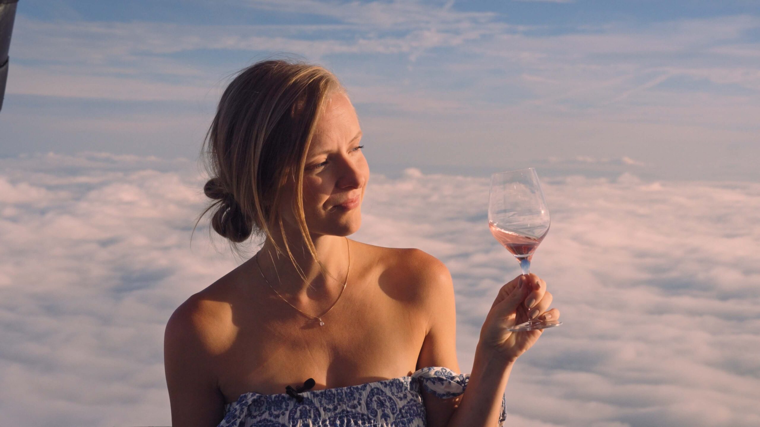 Rioja Paired host Marti Buckley holding a glass of rosé against a cloud-filled landscape