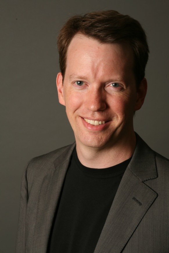 Sean Carroll in a dark jacket, photographed against a neutral background